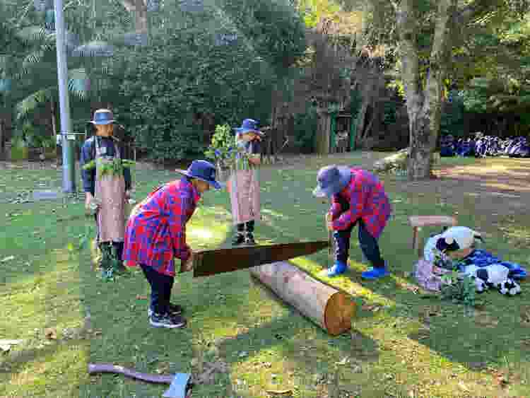 Two students dressed as trees and two students dressed as cedar fellers who are together sawing a log with a bandsaw.