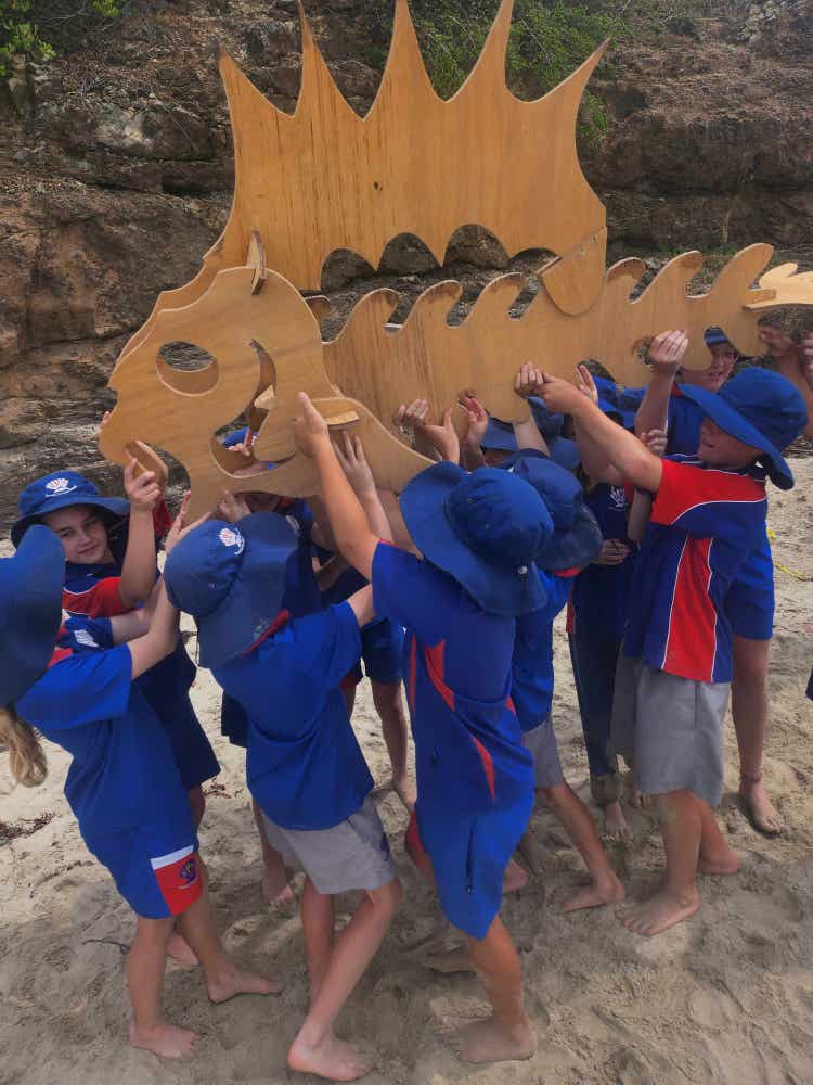 Group of students on beach holding up a reconstructed model of a prehistoric fish