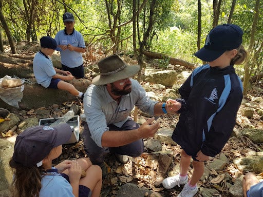 Teacher assisting a young student with a clay creature in the rainforest