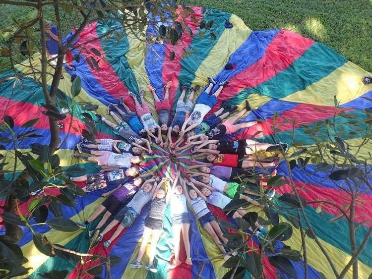 Large colourful parachute with students arranged around in a cicle on their backs